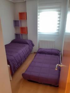 1 dormitorio con camas de color púrpura y ventana en El pisito de Irene, en Béjar