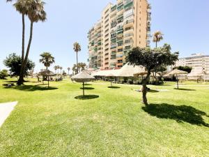 un parque con palmeras y sombrillas y un edificio en Estudio Nuevo con Vistas al Mar en Benalmádena Costa, en Benalmádena