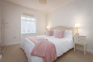 a white bedroom with a large bed with pink pillows at Charles Alexander Short Stay - Rose Cottage in Lytham St Annes