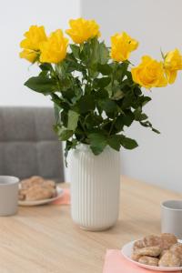 a white vase filled with yellow roses on a table at Metro Bielany Apartments with Parking by Renters in Warsaw