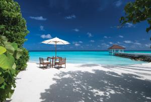 a table with chairs and an umbrella on a beach at VARU by Atmosphere - Premium All Inclusive with Free Transfers in North Male Atoll