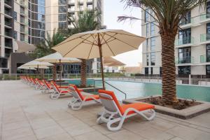 eine Reihe von Stühlen und Sonnenschirmen neben einem Pool in der Unterkunft Expo Village Serviced Apartments in Dubai