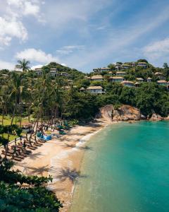 a beach with chaise lounges and palm trees at Banyan Tree Samui in Lamai