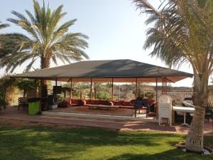 een prieel met een tafel en stoelen en palmbomen bij The Dunes Farm House RAK in Masāfī