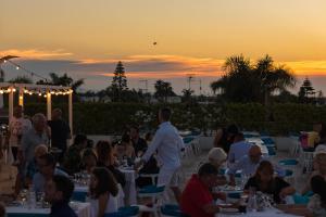 a group of people sitting at tables at sunset at Riva Marina Resort - CDSHotels in Carovigno