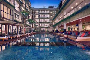 a large swimming pool in a building with chairs at Hotel NEO+ Kuta Legian by ASTON in Legian