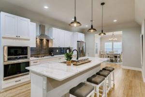 a kitchen with white cabinets and a large island with bar stools at NEW 4 BDRM Home off St Mary’s Mins To Pearl/River! in San Antonio