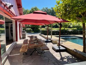 a patio with tables and a large red umbrella at Magnifique Villa avec Piscine-Jacuzzi-coin fitness in Bidart