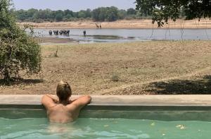 un hombre en una bañera en un cuerpo de agua en Msandile River Lodge, en Kakumbi