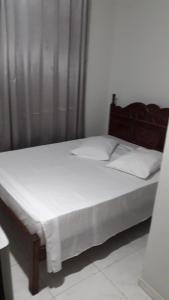 a bed with white sheets and a wooden headboard at Pousada Nova in Montes Claros