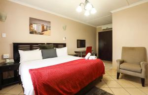 a bedroom with a bed with a red blanket and a chair at Nongoma Lodge & Inn CC in Nongoma