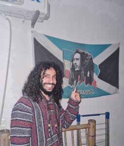 a man with long hair giving a thumbs up in front of a flag at Merabi Guest House in Makhinjauri