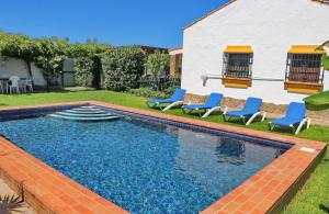 a swimming pool with blue chairs and a house at Chalet Dehesa Villa in Conil de la Frontera