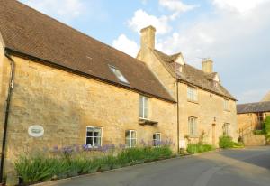 an old brick building with purple flowers in front of it at Cotswold Charm George Barn in Chipping Campden