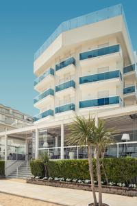 a white building with palm trees in front of it at Hotel Atlantico in Lido di Jesolo