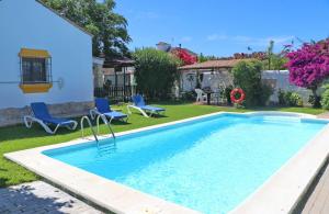 a swimming pool in a yard with blue chairs and a house at Chalet la Dehesa in Conil de la Frontera
