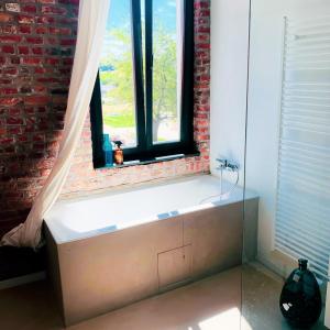 Cette chambre dispose d'une fenêtre avec une baignoire et d'un mur en briques. dans l'établissement Little Farm Comfort&PrestigeHouse, à Ittre