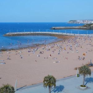 a beach with a lot of people in the water at Apartamento chile playa in Gijón