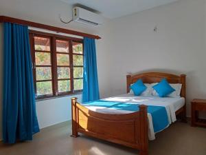 a bedroom with a bed with blue curtains and a window at Palmeiral BeachVilla in Calangute