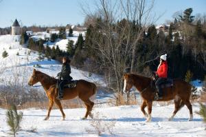 two people riding on horses in the snow at Le Baluchon Éco-villégiature in Saint-Paulin