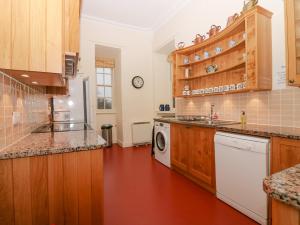 cocina con armarios de madera, lavadora y secadora en The Preston Tower Apartment - Fyvie Castle, en Turriff