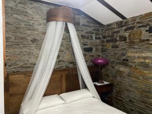 Una cama con dosel en una habitación con una pared de piedra. en Casas Rurales TAReira en Taramundi, en Taramundi