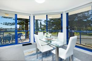 a dining room with a glass table and white chairs at Heritage 201 in Tuncurry