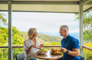 Ein Mann und eine Frau sitzen an einem Tisch mit einem Teller Essen. in der Unterkunft Binna Burra Rainforest Campsite in Beechmont