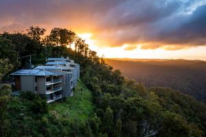 a building on a hill with the sunset in the background at Binna Burra Sky Lodges in Beechmont +18 photos