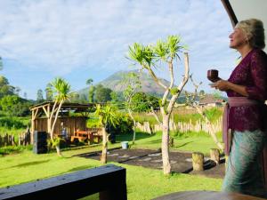 a woman standing in a yard holding a cup of coffee at Batur Homestay and Lodge in Bangli