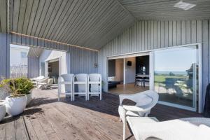 eine Terrasse mit weißen Stühlen, Tischen und Glastüren in der Unterkunft Luxury Ocean Villa in Papamoa in Papamoa