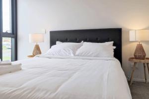 a large white bed with white pillows and two lamps at Brand new stylish 2BR apartment- free parking in Auckland