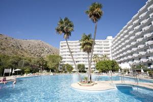 a swimming pool with palm trees and a large building at Apartamentos Siesta I in Port d'Alcudia