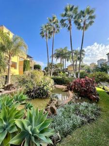 een tuin met palmbomen en een vijver met planten bij Ático nuevo en lujosa urbanización junto a restaurantes y cafeterías in Marbella