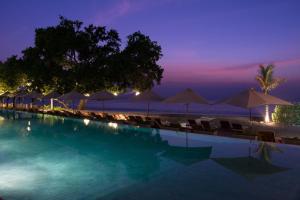 a pool with chairs and umbrellas on the beach at night at Living Asia Resort and Spa in Senggigi