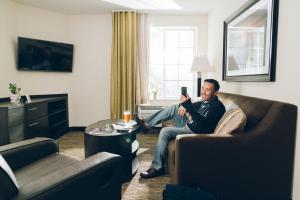 un hombre sentado en un sofá en una sala de estar con su celular en Candlewood Suites - Dumfries - Quantico by IHG, en Dumfries
