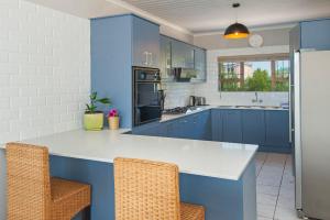 a kitchen with blue cabinets and a counter with two chairs at Sunrise Bettys Bay in Bettyʼs Bay