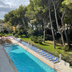 a swimming pool with lounge chairs and trees at Guya Wave Hotel in Cala Ratjada