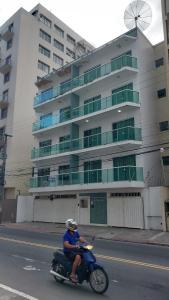 un uomo che guida uno scooter lungo una strada di fronte a un edificio di Apartamento confortável no centro de Guarapari a Guarapari