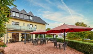 un patio con mesas, sillas y sombrillas rojas en Hotel Café Ernst, en Bernkastel-Kues