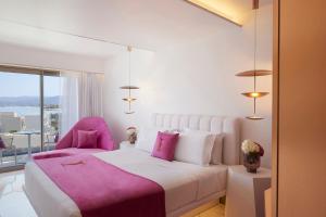 a bedroom with a white bed and two pink chairs at I Resort Beach Hotel & Spa in Stalida