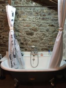 a bath tub with a shower curtain in front of a stone wall at Casa de Aldea Ecocorneyana in Campomanes