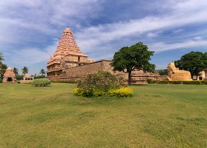 a building in a field with a tree in the foreground at Marudhan Grand in Kumbakonam