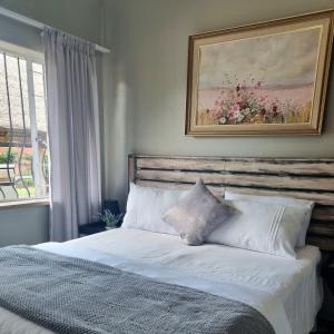 a bedroom with a white bed with a painting on the wall at Isabel's B & B in Krugersdorp