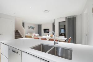 a white kitchen with a sink and a living room at Nexus Townhouse with Parking and Wi-Fi in Auckland