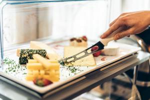 Eine Person, die ein Messer auf einem Teller mit Käse hält. in der Unterkunft Aktivhotel Wildschütz in Gmunden