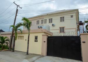 a white house with a black gate and a palm tree at YP George in Lekki