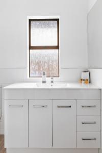 baño blanco con lavabo y ventana en Cobblestone Court Motel - Wenzel Motels, en Tauranga