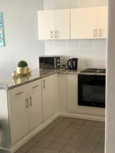 cocina con armarios blancos y microondas negro en T' Primage Suite on Ten South, en Durban