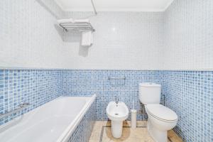 a blue tiled bathroom with a toilet and a bath tub at Yellow Praia Monte Gordo in Monte Gordo